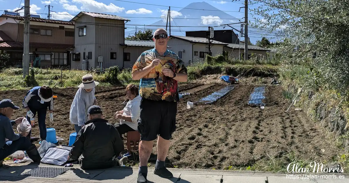 Alan Morris eating ice cream, next to him locals take a break from sowing rice. Mount Fuji is in the background.